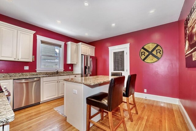 kitchen featuring light stone counters, stainless steel appliances, a center island, and white cabinets