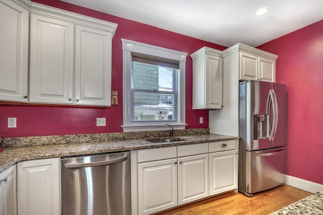 kitchen featuring sink, light hardwood / wood-style flooring, appliances with stainless steel finishes, white cabinetry, and dark stone counters