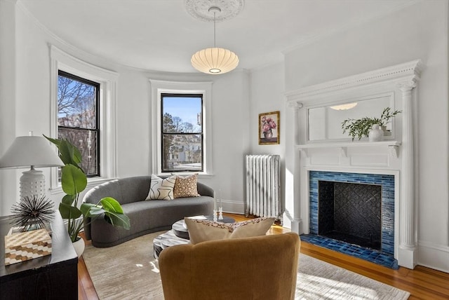 living room with ornamental molding, wood finished floors, radiator, a fireplace, and baseboards