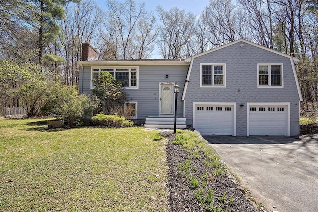 bi-level home featuring an attached garage, a chimney, asphalt driveway, and a front yard