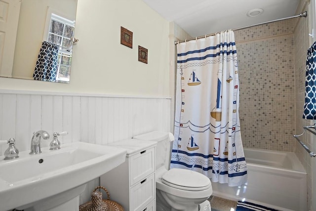 full bath with a sink, toilet, shower / tub combo, and a wainscoted wall