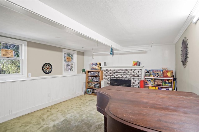 home office with carpet, a brick fireplace, a textured ceiling, crown molding, and wainscoting