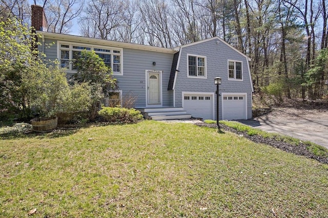 raised ranch featuring a garage, asphalt driveway, a chimney, and a front yard