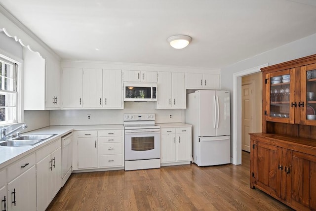kitchen with white appliances, a sink, light countertops, wood finished floors, and white cabinetry