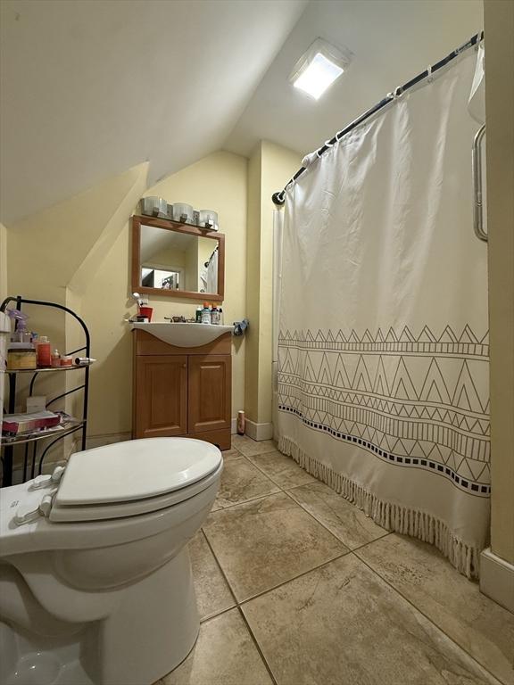 bathroom featuring toilet, vaulted ceiling, vanity, a shower with curtain, and tile patterned floors