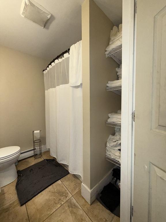 bathroom with a baseboard radiator, toilet, a shower with shower curtain, visible vents, and baseboards