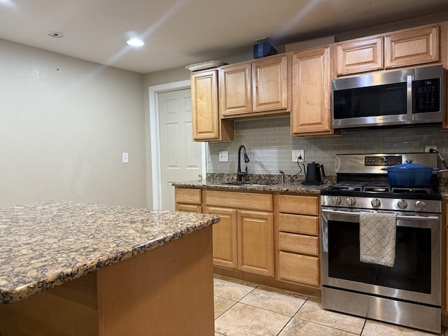 kitchen featuring light tile patterned floors, decorative backsplash, appliances with stainless steel finishes, dark stone countertops, and a sink