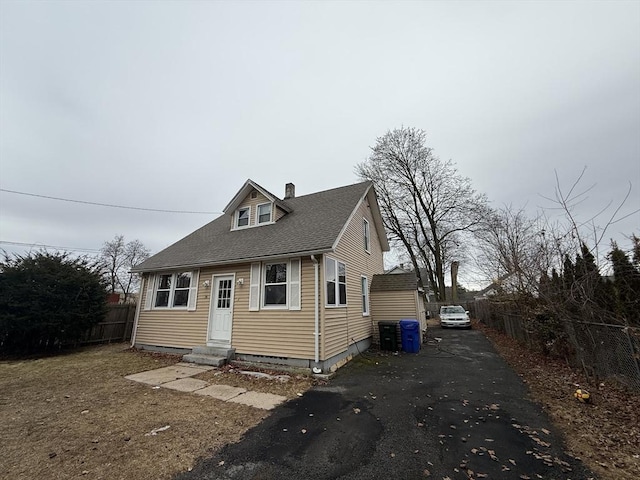 view of front of house featuring a shingled roof, entry steps, fence, and a chimney