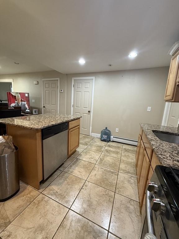 kitchen with a kitchen island, baseboard heating, stainless steel appliances, stone counters, and a sink