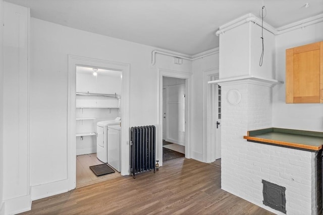 kitchen with dark wood-type flooring, washing machine and clothes dryer, radiator heating unit, and light brown cabinets