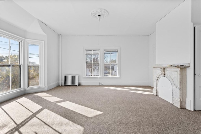 unfurnished living room with plenty of natural light, radiator, and carpet