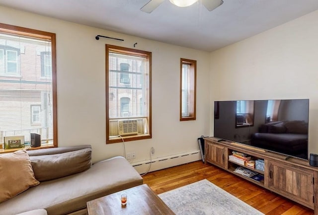 living area with a baseboard heating unit, healthy amount of natural light, wood finished floors, and ceiling fan