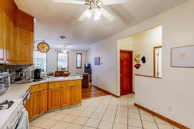 kitchen featuring a ceiling fan, a peninsula, light countertops, a sink, and stove