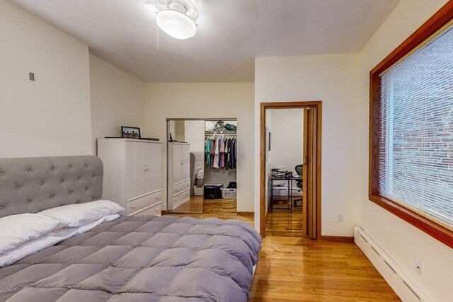 bedroom with a baseboard radiator, light wood-style floors, and a closet