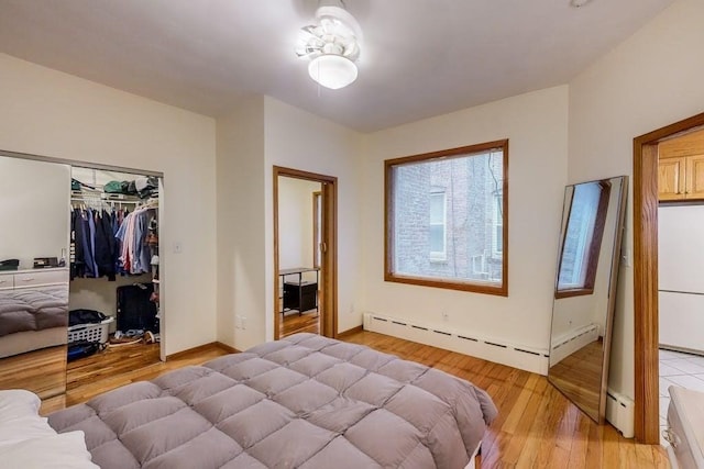 bedroom featuring a baseboard heating unit, a baseboard radiator, light wood-style floors, baseboards, and a closet
