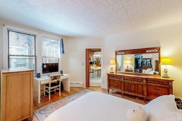 bedroom featuring a baseboard radiator, wood finished floors, and a desk