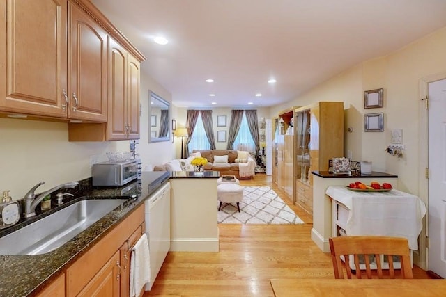 kitchen with a sink, light wood-style floors, white dishwasher, open floor plan, and dark stone countertops