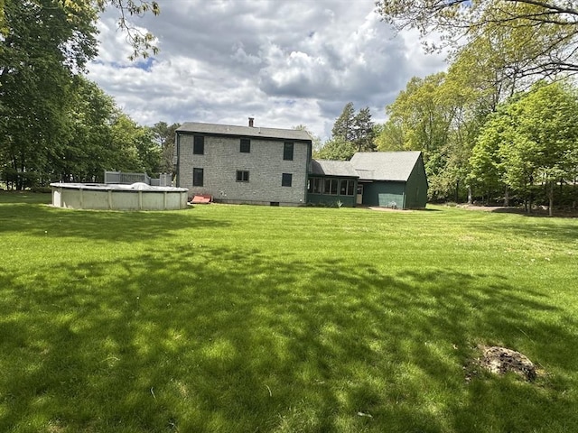rear view of property with a covered pool, a yard, and view of wooded area