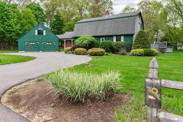 colonial inspired home with a gambrel roof, roof with shingles, a garage, a front lawn, and a chimney