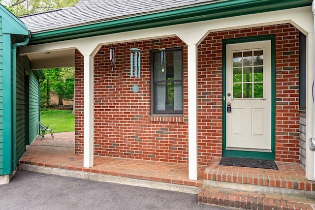view of exterior entry with brick siding and covered porch