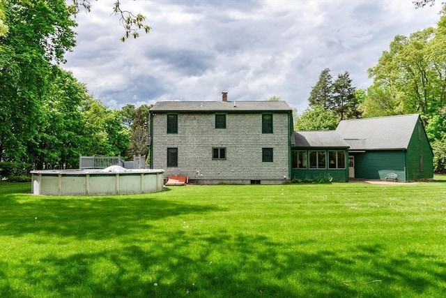 rear view of house with a covered pool, a chimney, and a yard
