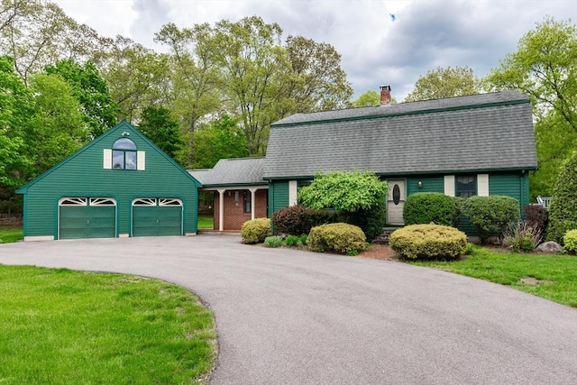 dutch colonial featuring a gambrel roof, driveway, a chimney, a shingled roof, and a front yard