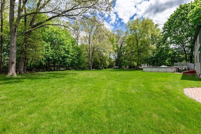 view of grassy yard with a covered pool and view of wooded area