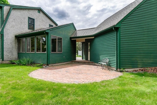 back of house featuring a patio, a yard, roof with shingles, and a sunroom