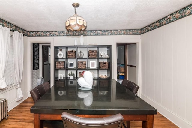 dining space with radiator heating unit, wood-type flooring, and a textured ceiling