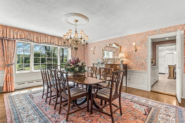 dining room featuring a textured ceiling, a chandelier, wainscoting, wallpapered walls, and wood finished floors