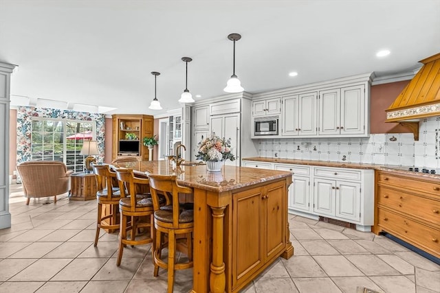 kitchen with stainless steel microwave, tasteful backsplash, light stone counters, light tile patterned floors, and recessed lighting