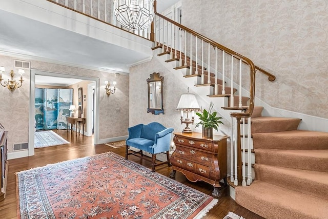 stairway with wallpapered walls, wood finished floors, ornamental molding, and baseboards