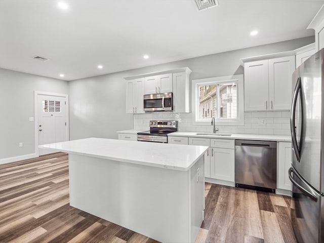 kitchen with appliances with stainless steel finishes, a center island, white cabinetry, and wood-type flooring