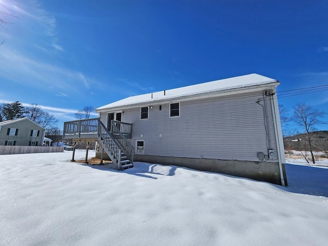 snow covered house with a wooden deck and stairs