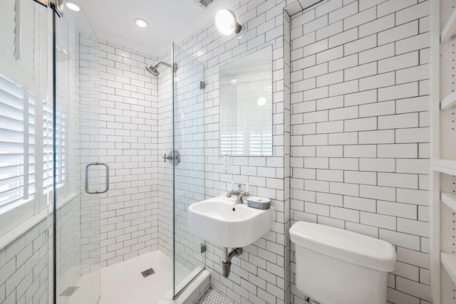 bathroom with tile walls, sink, a shower with shower door, and toilet