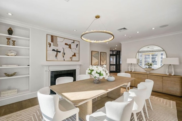 dining area with hardwood / wood-style floors, built in features, a tile fireplace, and ornamental molding