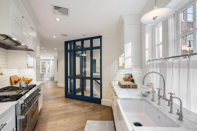 kitchen featuring pendant lighting, sink, light hardwood / wood-style flooring, white cabinets, and range with two ovens