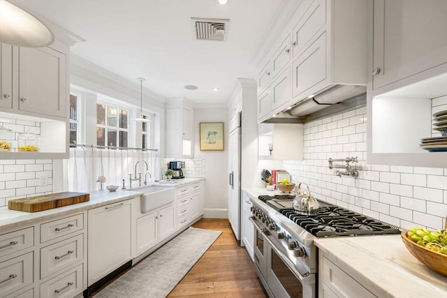 kitchen with sink, white cabinetry, hanging light fixtures, light stone counters, and range with two ovens