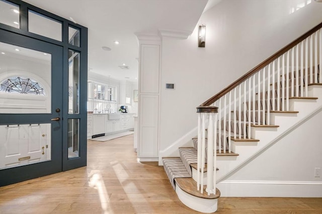 foyer entrance featuring crown molding, sink, and light wood-type flooring