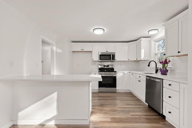 kitchen with appliances with stainless steel finishes, sink, white cabinets, and light wood-type flooring