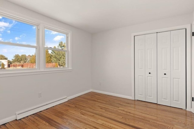 unfurnished bedroom with a baseboard heating unit, light wood-type flooring, and a closet