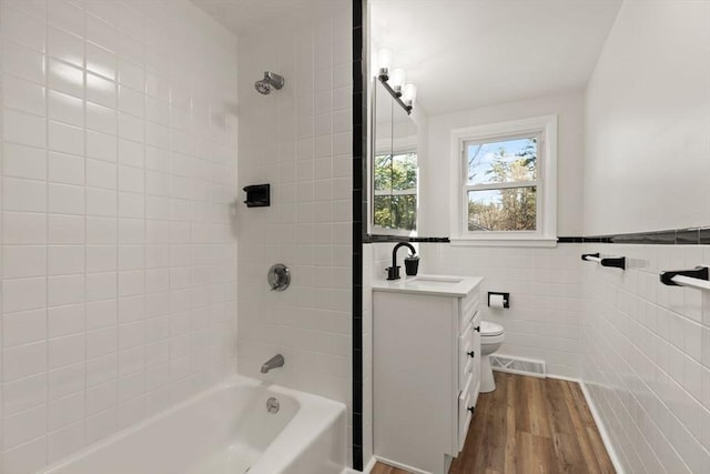 full bathroom with toilet, wood-type flooring, tile walls, vanity, and tiled shower / bath combo