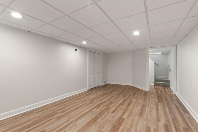 basement with a drop ceiling and light hardwood / wood-style flooring