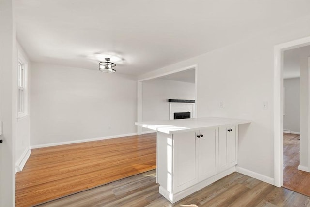 kitchen featuring light hardwood / wood-style flooring, white cabinetry, a fireplace, a kitchen bar, and kitchen peninsula