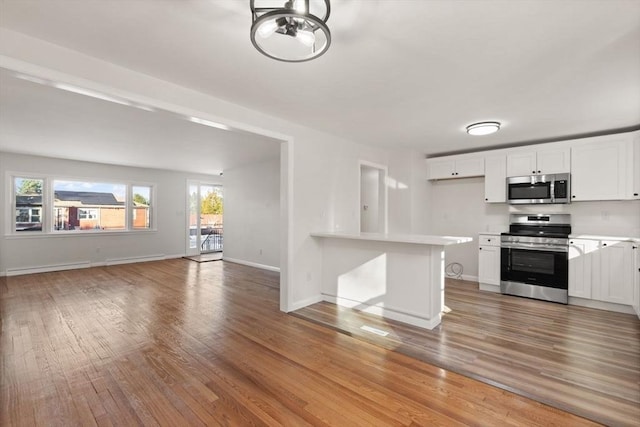 kitchen featuring a kitchen bar, white cabinetry, kitchen peninsula, hardwood / wood-style flooring, and stainless steel appliances