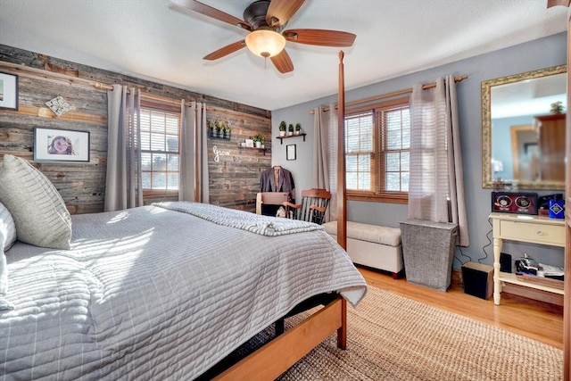 bedroom with ceiling fan, wooden walls, and light hardwood / wood-style flooring