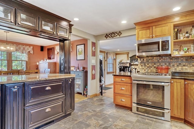 kitchen with appliances with stainless steel finishes, dark stone countertops, backsplash, and an inviting chandelier