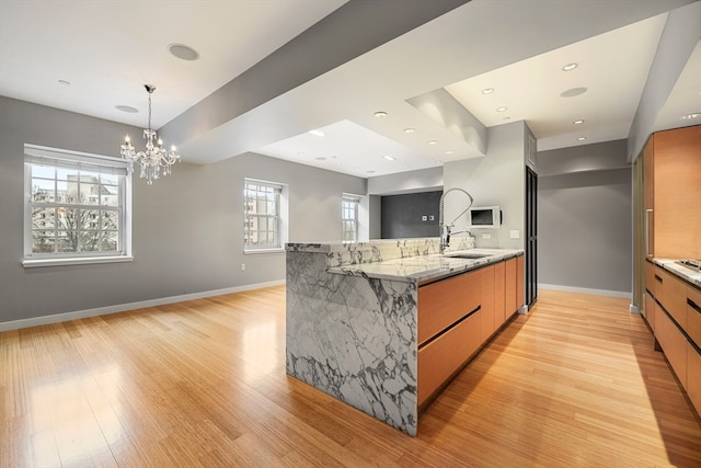 kitchen with light hardwood / wood-style flooring, a notable chandelier, light stone counters, hanging light fixtures, and sink