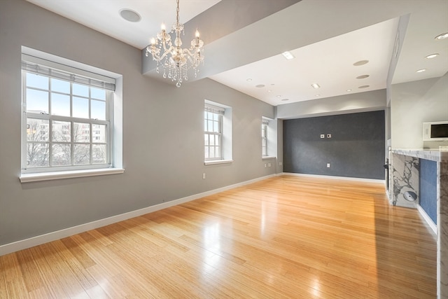 unfurnished living room featuring an inviting chandelier and light hardwood / wood-style floors