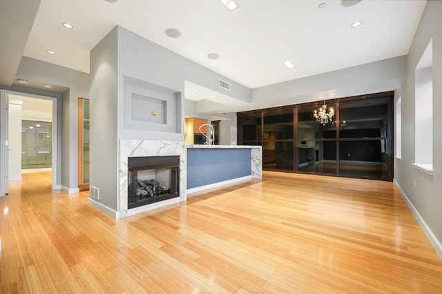 unfurnished living room with a premium fireplace, an inviting chandelier, and light hardwood / wood-style flooring